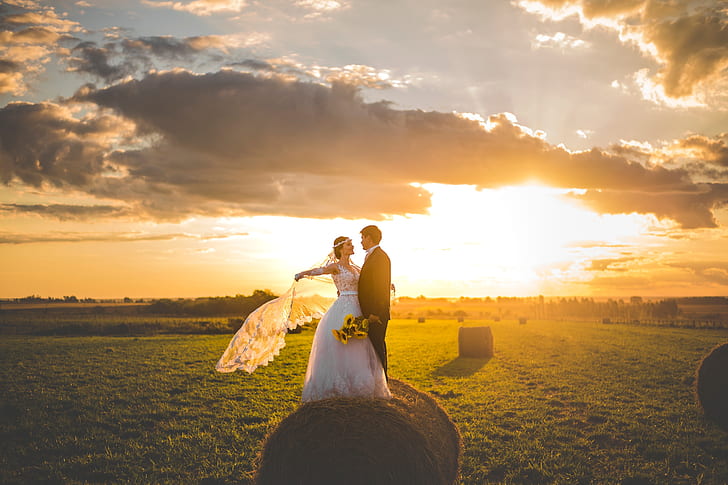 bride and groom taking picture on pale of hay under horizon