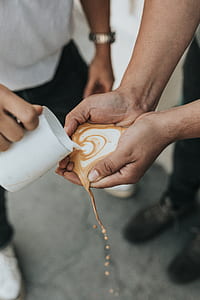 person pouring coffee latte on person's hands selective focus photography