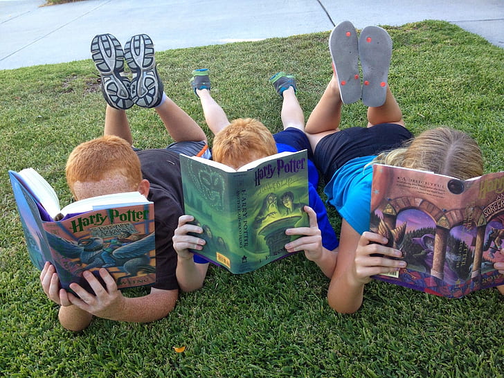 three childrens holding Harry Potter books while laying on grass photograph