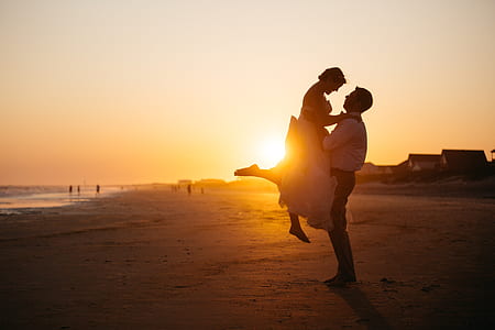 man and woman standing on seashore at golden hour photo