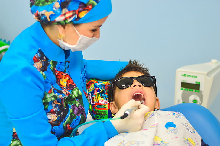 dentist checking boy's teeth wearingblack sunglasses