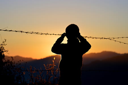 Silhouette of Boy Standing Near Barbed Wire