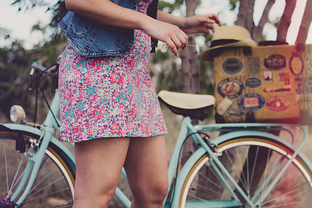 woman wearing blue denim top and floral multicolored mini dress standing near teal bicycle