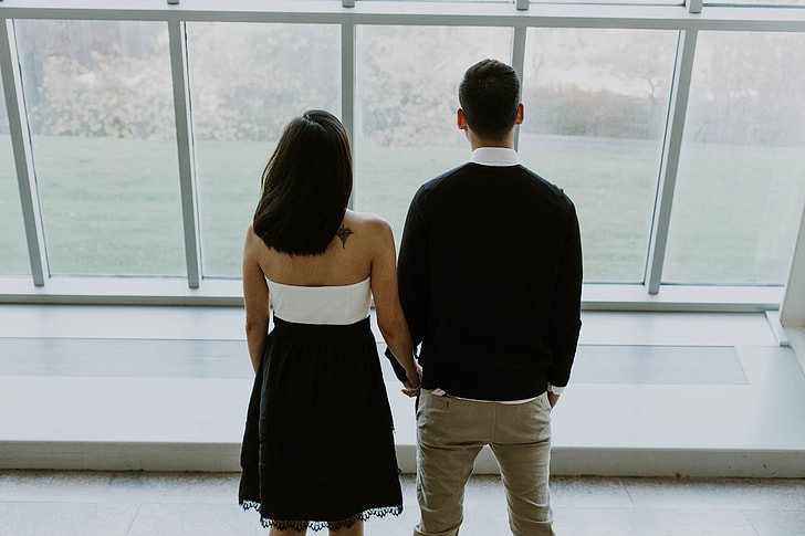 A young couple standing by large windows
