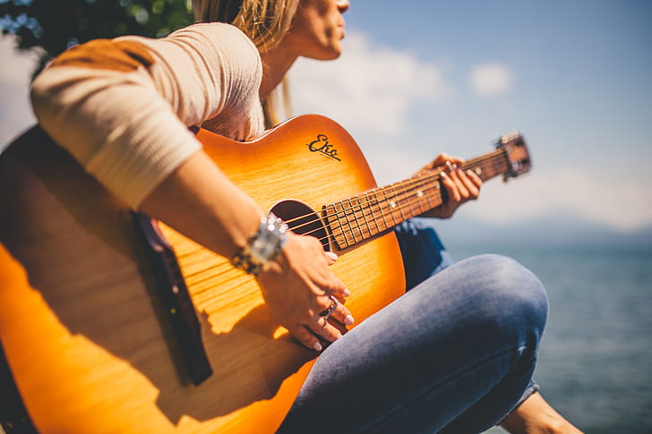 woman wearing sweatshirt playing acoustic guitar