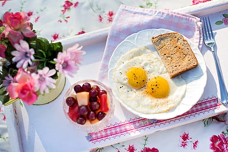 fried egg and sliced bread on plate beside cup of fruits