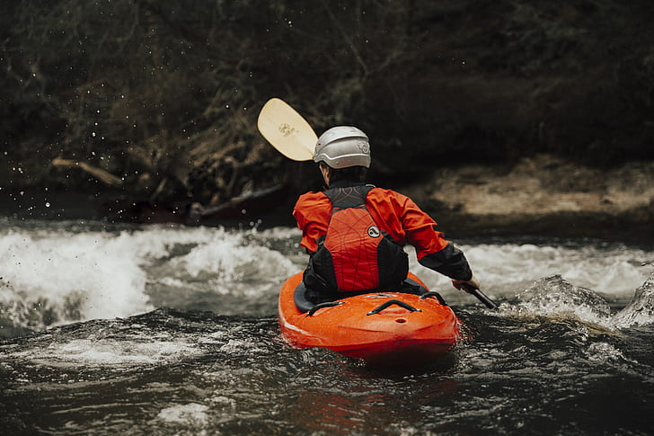man wearing gray helmet kayaking on flowing stream