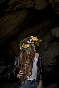 woman in black leather biker jacket with yellow hibiscus flower headdress standing near grey making post during daytime