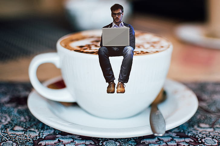 man in blue jacket using laptop above white teacup with saucer