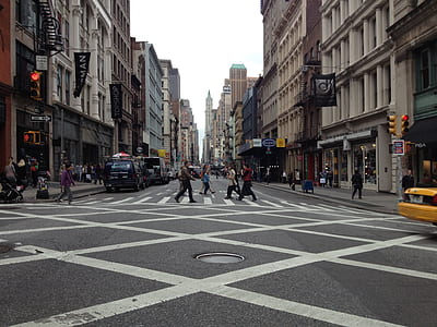 people crossing at the street between tall buildings during daytime