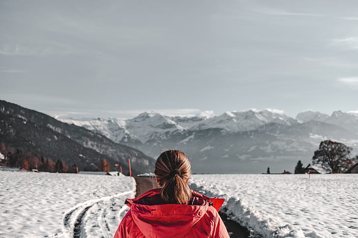 woman wearing red hoodie jacket standing in front of mountain