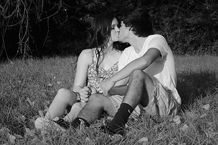 grayscale photo of couple sitting on grass while kissing