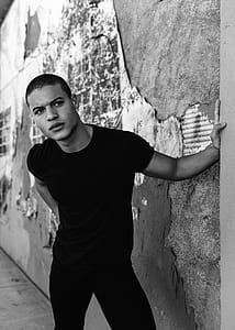 grayscale photo of man in shirt leaning on wall