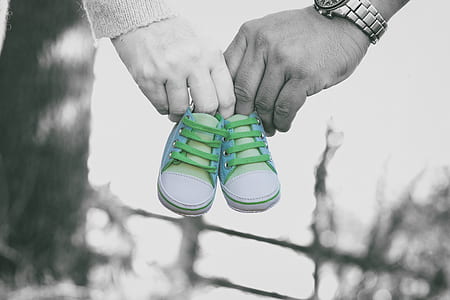 selective color photo of man and woman holding white-and-gray baby shoes
