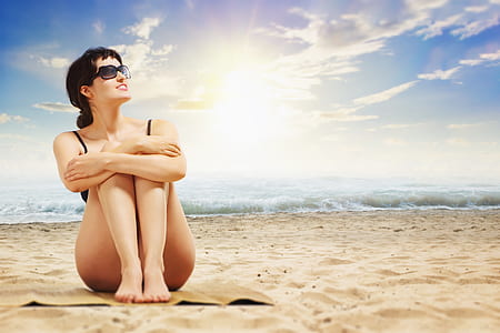 woman in black bikini sitting on brown sand