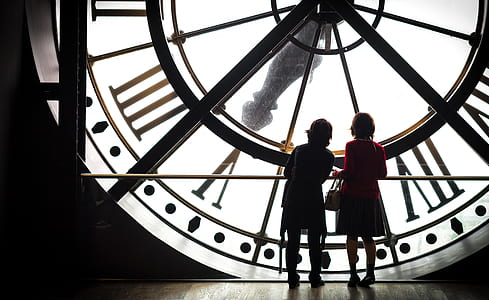 silhouette view of two women standing in front of big clock