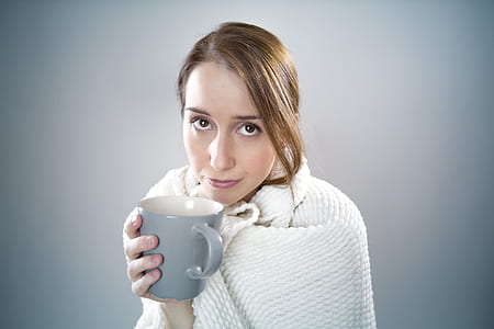woman with white blanket holding gray ceramic mug