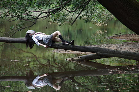 woman in white long-sleeved shirt lying on branch of tree during daytime