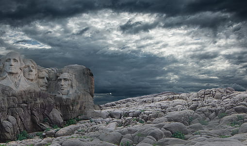 rock human head embossed mountain under gray and white cloudy sky during daytime