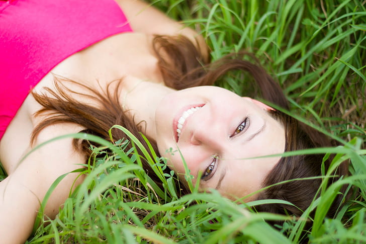 woman in pink strapless shirt lying on grass field during daytime