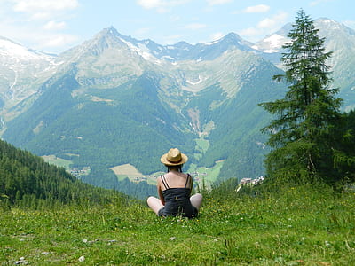 man wearing black spaghetti strap dress sitting on grass watching mountain range