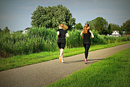 two women in black tops and bottoms running on grey trail
