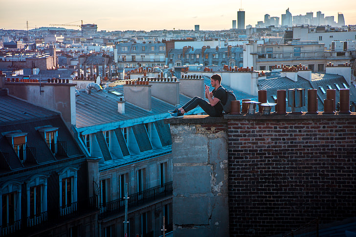 aerial photo of man sitting on rooftop ledge during daytime