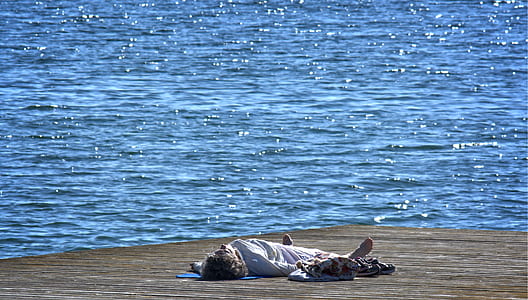 man in white long-sleeved shirt lying on brown sand near body of water during daytime
