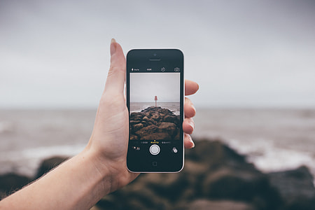 person holding black iPhone 4 while taking photo of sea shore during daytime