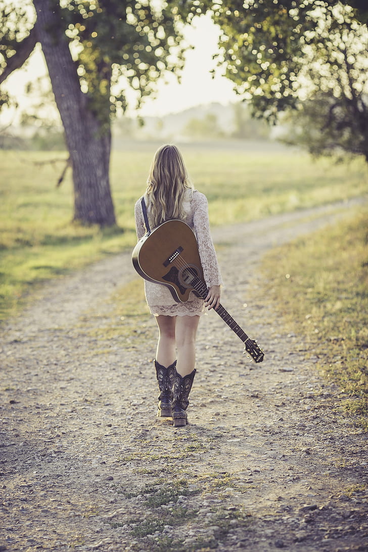 walking woman holding brown guitar at daytime