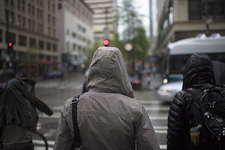 selective focus photography of human wearing gray leather hooded coat while crossing on pedestrian lane during daytime