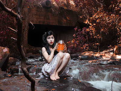 woman holding jar while sitting on stone with water flowing background at daytime