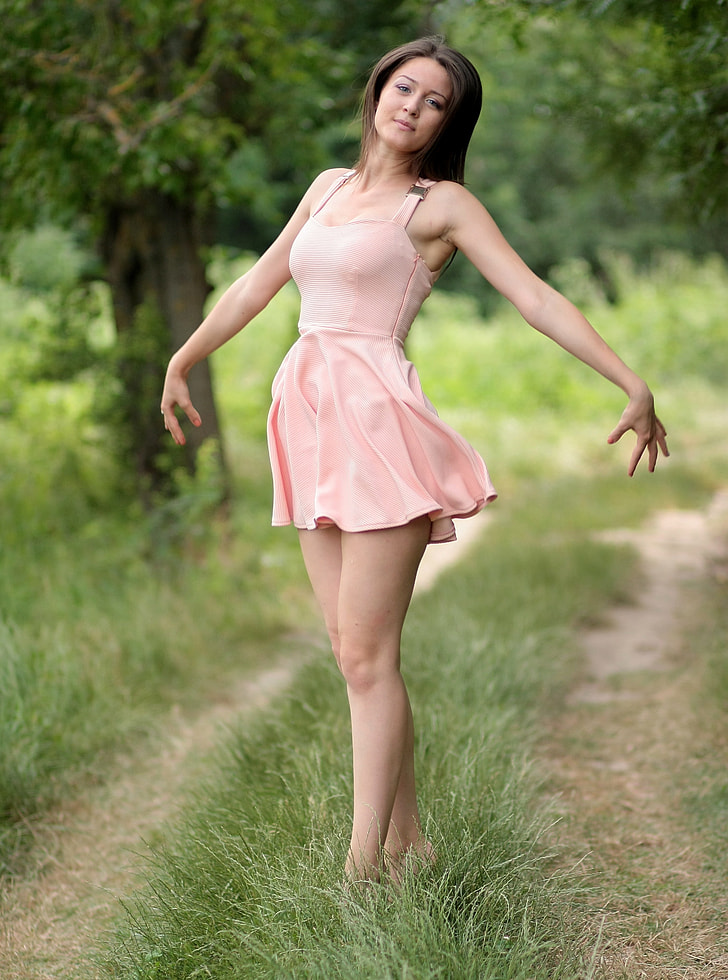 woman wearing pink sleeveless mini dress standing on green grass