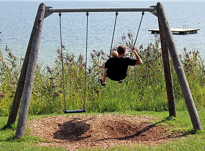 man in black shirt riding swing during daytime