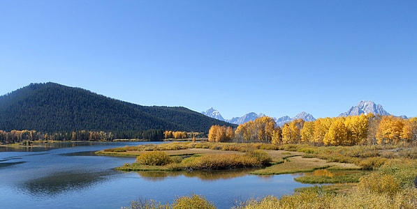 wide angle photo of body of water and green mountain under blue sky