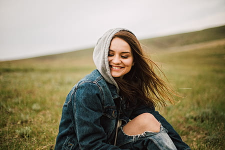 panning photography of female wearing blue denim hoodie while sitting on green grass field