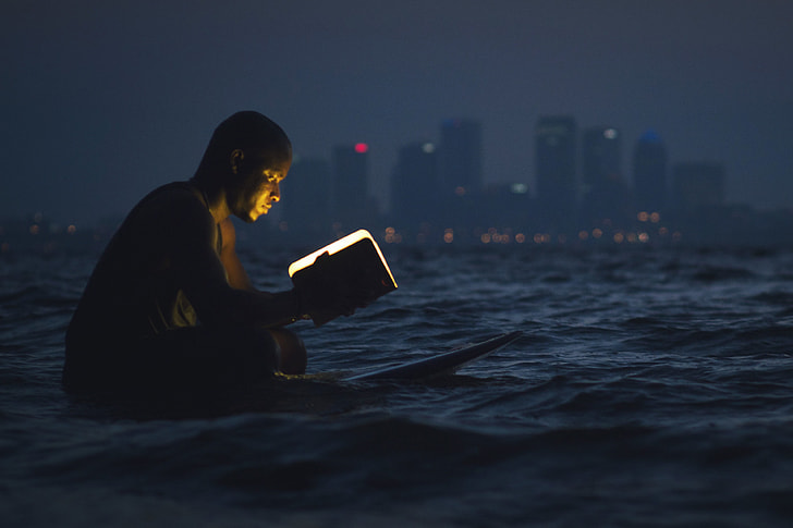 Man reading a book in the ocean at night
