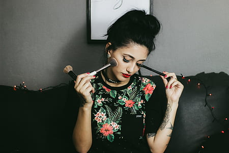 woman holding makeup brush while sitting on black sofa