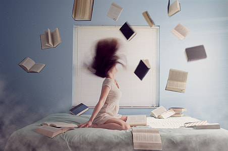 woman in white dress throwing assorted books while whipping her hair on bed