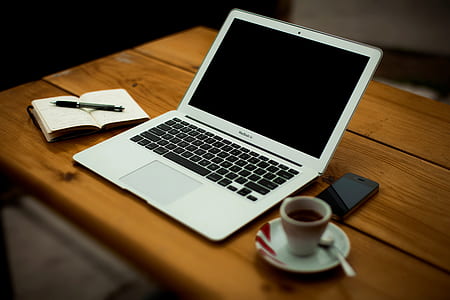 MacBook Air on brown wooden table beside white ceramic teacup and saucer