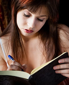 woman holding blue ballpoint pen and black book