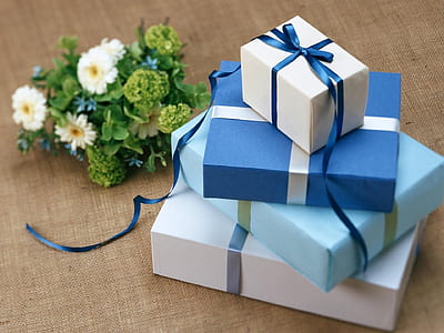 stack of four assorted-color gift boxes beside white and green petaled flower bouquet