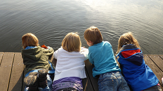 four children proning on brown harbor dock at daytime