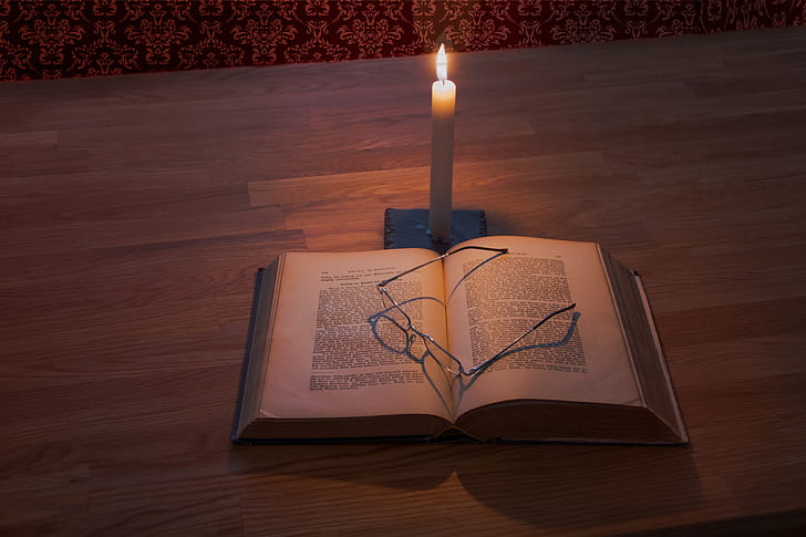 white taper candle and book on brown wooden table