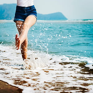 woman barefoot on beach kicking waters at daytime