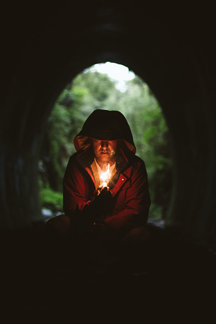 man wearing brown hooded jacket lighting a match in tunnel