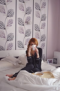 woman wearing piping-white black pajama set holding white ceramic mug sitting on white bedspread set