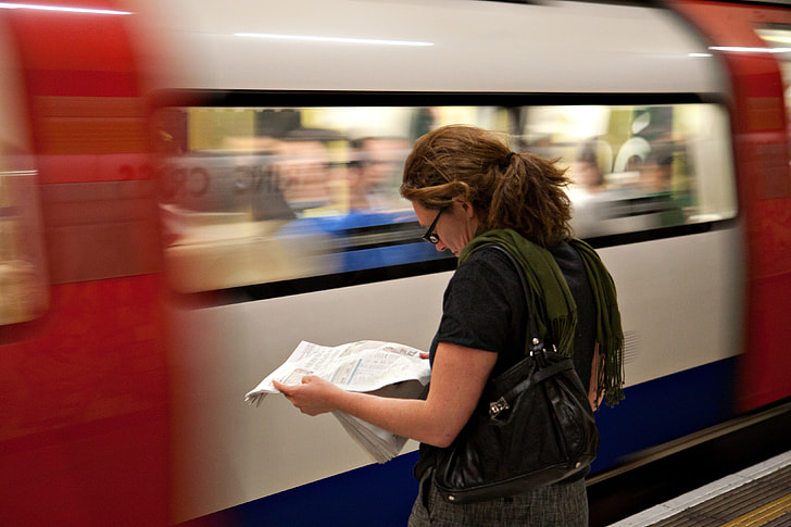 A woman reads the newspaper as she waits for her connection on the London Underground