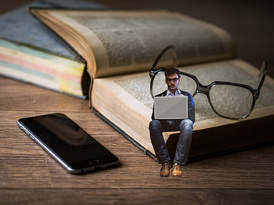 man with laptop edited photo sitting on book with eyeglasses near black iPhone 7