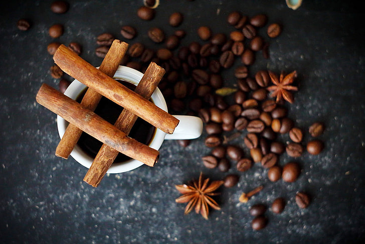 shallow focus of brown coffee beans beside white ceramic mug